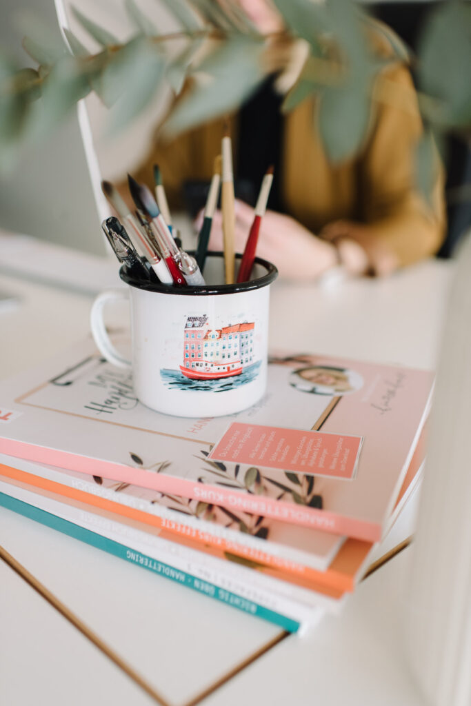 Stilleben auf dem Schreibtisch mit Stiften in einer Tasse und einem Stapel Magazinen